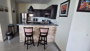 Uma cozinha moderna com ilha central, armários escuros e dois bancos.