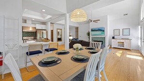 Un comedor moderno con una mesa de madera dispuesta para seis personas, sillas blancas y una araña.