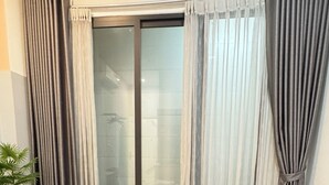 Habitación de hotel con cama, una mesita con una planta y un ventanal con cortinas.