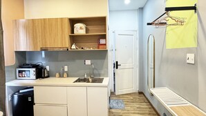 Cocina compacta con microondas, pileta y un refrigerador pequeño. Hay un mueble de madera sobre la encimera y una puerta blanca cerca.