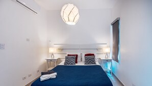 Et moderne hotelværelse med en stor seng, to sengeborde med lamper, en loftslampe og et vindue med gardiner.
