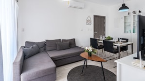 En moderne stue med en grå hjørnesofa, et træsofabord og et spiseområde med et hvidt bord og sorte stole.