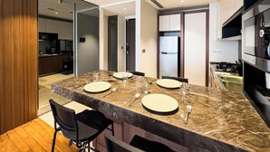 Un comedor moderno con encimera de mármol, sillas negras y una cocina al fondo.