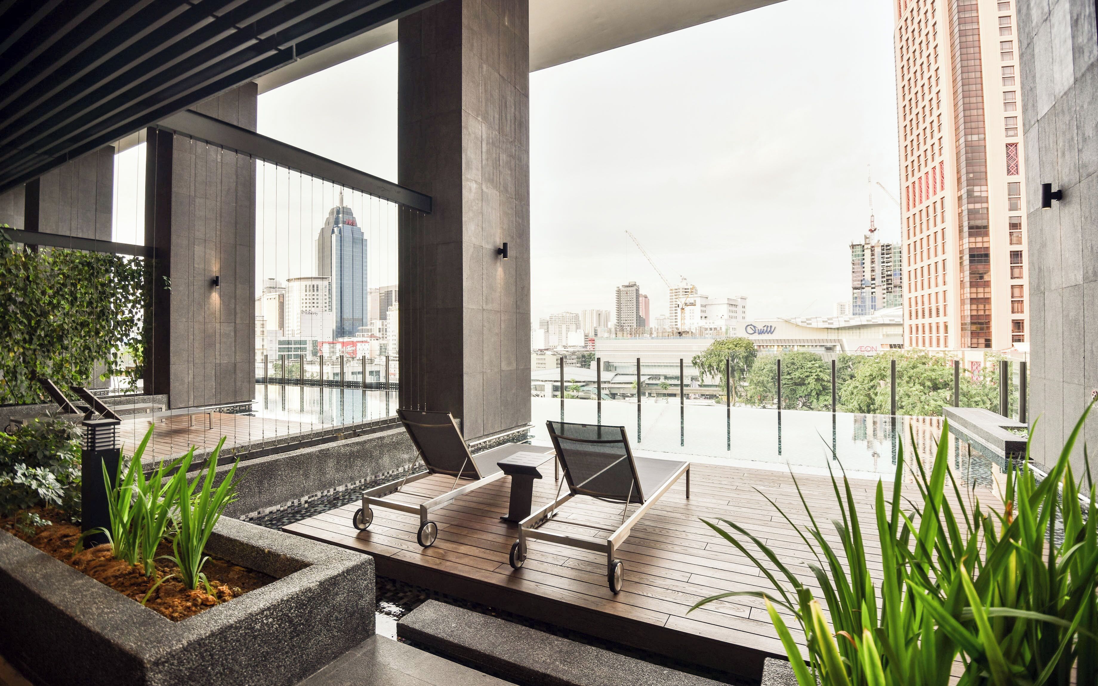 Un espace de détente extérieur moderne avec vue sur les gratte-ciel de la ville, comprenant une terrasse en bois, des fauteuils et des jardinières.