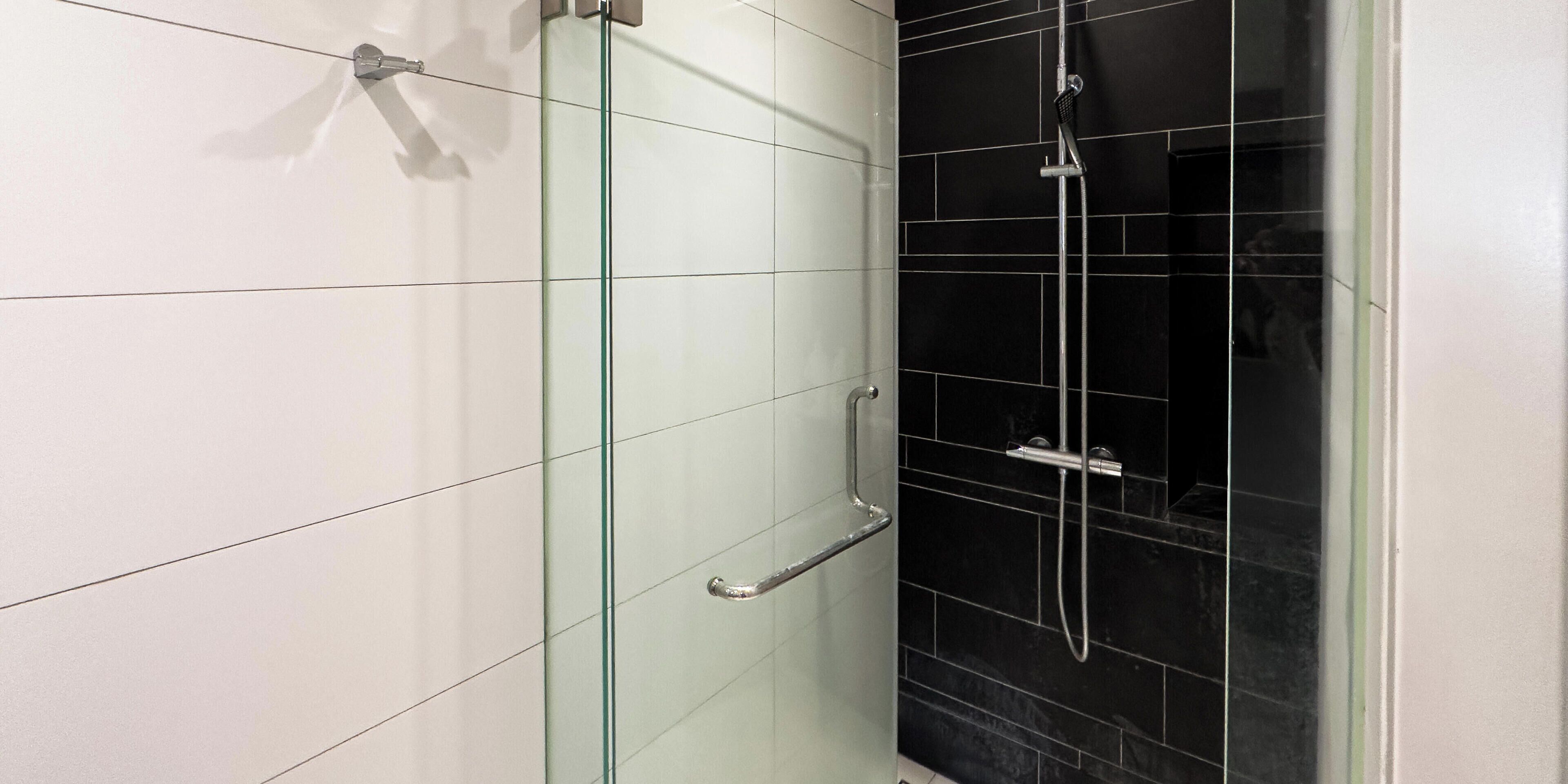 Un baño moderno con cabina de ducha de vidrio, pared de azulejos negros y suelo de baldosas blancas.