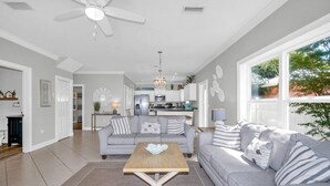 Ein geräumiges Wohnzimmer mit einem grauen Sofa, einem Holztisch und einer Küche im Hintergrund.
