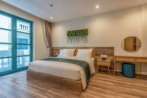 A modern hotel room with a large bed, a desk, a chair, a round mirror, and a view of the outside balcony. - La Vita Bliss Phu Quoc (Duong To)