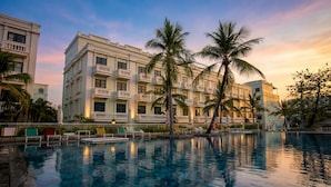 Un hôtel avec une piscine, des palmiers et une vue sur le coucher de soleil.