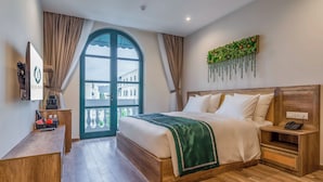 Une chambre d’hôtel avec un grand lit, des tables de chevet en bois, un bureau et une vue sur l’extérieur, visible à travers une porte vitrée.
