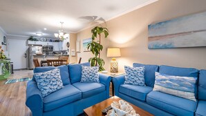 Ein Wohnzimmer mit zwei blauen Sofas, einem Couchtisch, einer Lampe und einem Gemälde an der Wand.