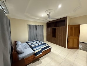 Een slaapkamer met een bed, gordijnen, een plafondventilator en houten kasten.