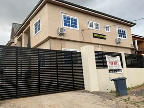 Een gebouw met twee verdiepingen, een beige gevel, een zwart hek en een bord waarop kortetermijnverhuur wordt aangeboden.