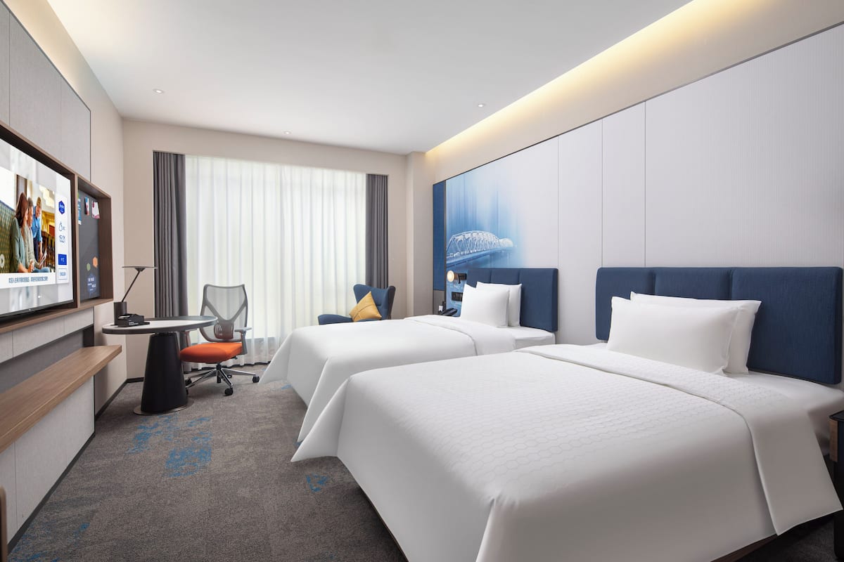 Ein Hotelzimmer mit zwei Betten, einem Schreibtisch, einem Stuhl und einem Fernseher.