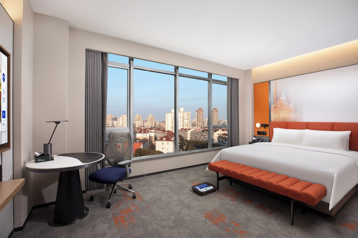 Ein Hotelzimmer mit großem Fenster, einem Bett, einem Schreibtisch und einem Sessel.