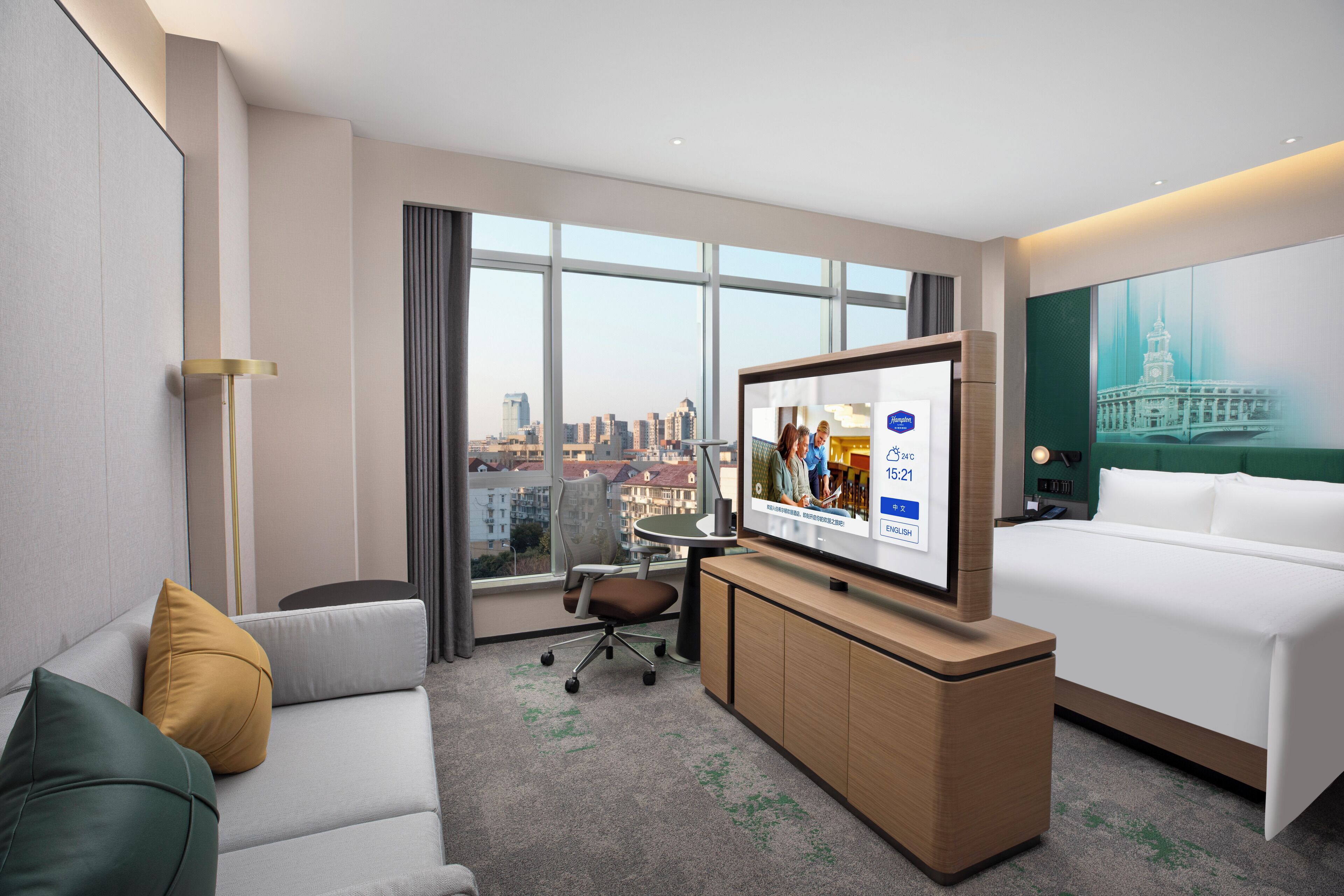Quarto de hotel com uma janela ampla, cama, sofá, televisão e escrivaninha.