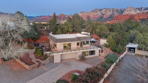 Une maison moderne à deux étages, dotée d’un balcon, entourée d’un jardin aménagé et offrant une vue sur des formations rocheuses rouges.