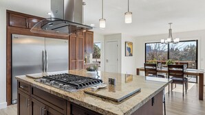Une cuisine moderne dotée d’un grand îlot central, d’appareils électroménagers en acier inoxydable et de luminaires suspendus.