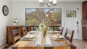 Un coin repas avec une table en bois dressée pour quatre personnes, un lustre et une vue sur un paysage montagneux par le biais d’une grande fenêtre.