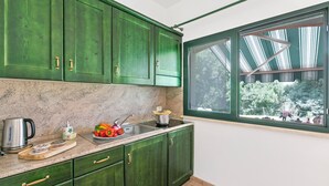 Ett kök med gröna skåp, en bänkskiva i marmor, ett fönster med utsikt över träd och en hängande lampa.