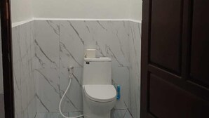 Un bany petit i compacte amb vàter blanc, parets amb dibuix de marbre i una porta de fusta fosca.