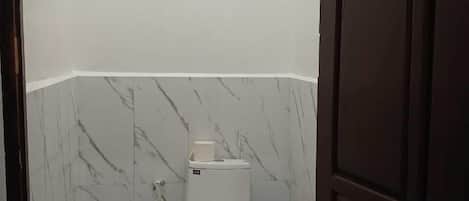 Un baño pequeño y funcional con inodoro blanco, paredes con diseño de mármol y puerta de madera oscura.