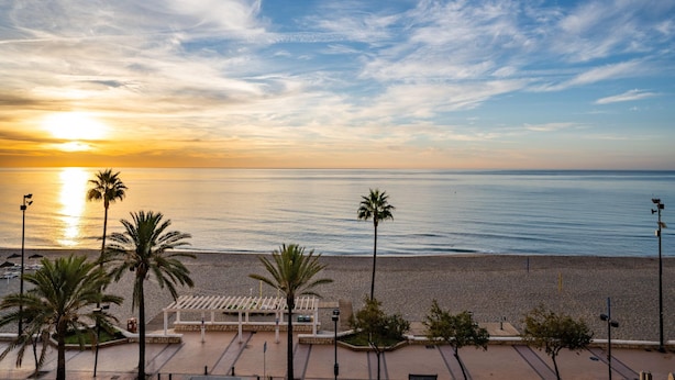 Blick auf einen Strand mit Sonnenuntergang, Palmen und einer weißen Laube.