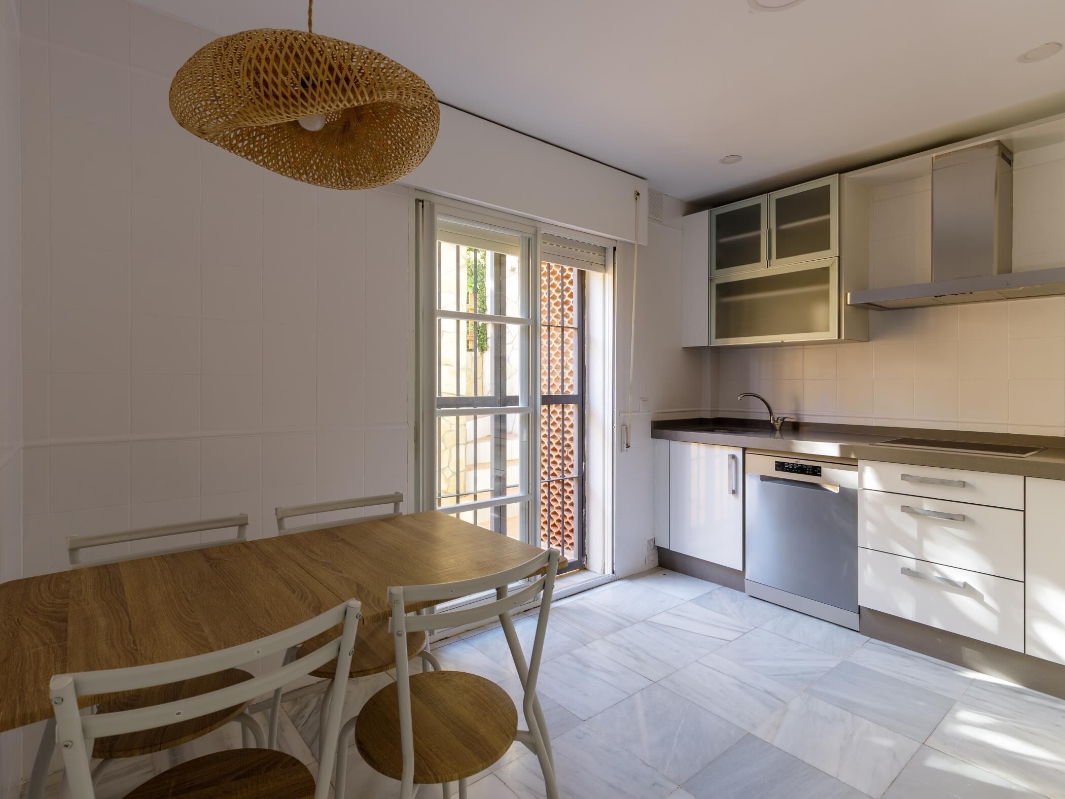 A modern kitchen with white cabinets, a stainless steel sink, and a dining area with a wooden table and white chairs.
