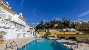 Una piscina amb rajoles de pedra, un edifici blanc amb balcons i una paret groga.