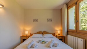 Ein ordentlich bezogenes Bett mit aufgerollten Handtüchern, einer Nachttischlampe und einem Fenster mit Vorhängen.