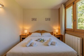 A neatly made bed with rolled towels, a bedside lamp, and a window with curtains. - Vallorcine Balme 15 ski in / ski out, Vallorcine (Argentiere), France (Vallorcine (Argentiere))