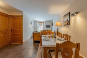 A dining area with a wooden table and chairs, a TV mounted on the wall, and a door leading to another room.