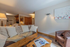 A cozy living room with a wooden sofa, a brown leather armchair, and a coffee table with a magazine and remote control.