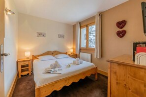 A bedroom with a wooden bed, bedside lamps, a window with curtains, and a dresser.