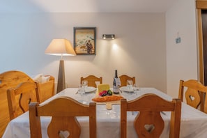 A dining table set with a bottle, glasses, a plate with cheese and grapes, and a heart-shaped cutout on the chair backs.