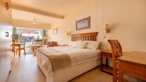 Ein Hotelzimmer mit einem großen Bett, einem Holznachttisch, einem Schreibtisch und einem Sessel. Ein Fenster mit Vorhängen bietet einen Blick nach draußen.