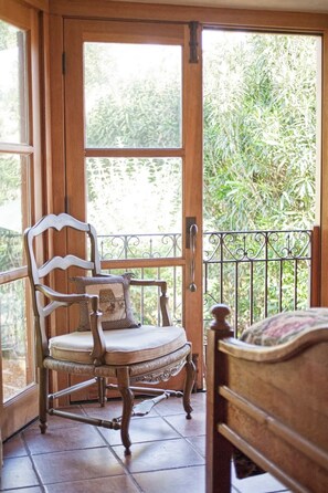 A wooden rocking chair with a cushion and a decorative pillow, positioned on a tiled floor near a wooden door with a glass panel.