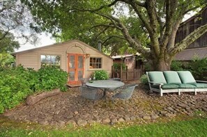 A rustic cabin with a stone patio, a dining table with chairs, and a green outdoor sofa.