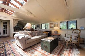 A spacious living room with a sofa, a coffee table, and a chair. There is a window with a view of greenery outside. - La Buona Stella Napa Valley (Saint Helena)