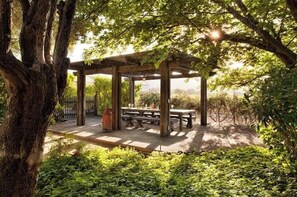 A covered outdoor seating area with tables and benches, surrounded by trees and greenery. - La Buona Stella Napa Valley (Saint Helena)