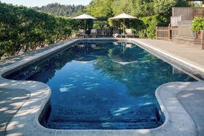 A rectangular swimming pool with a stone edge, surrounded by a wooden deck and two umbrellas. - La Buona Stella Napa Valley (Saint Helena)