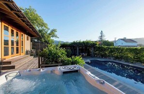 Een jacuzzi en een zwembad in een achtertuin met houten terrassen en een pergola.