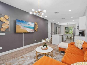 A modern living room with a large TV, a dining area, and a kitchen. - Super Calm- Sleeps 17 W Designs Close TO Parks (Kissimmee)
