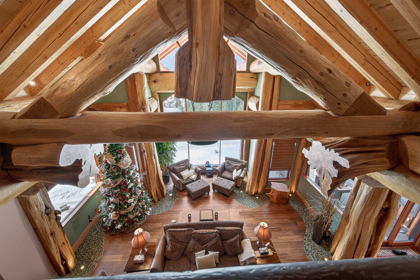 A log cabin interior with a high ceiling, wooden beams, a fireplace, and a Christmas tree.