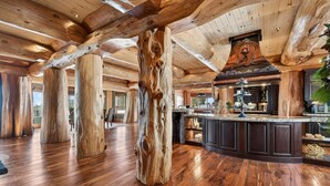 Amplia habitación con vigas de madera, una columna de madera grande y una zona de cocina con muebles oscuros y encimera.