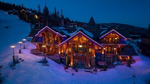 Un amplio hospedaje de varios pisos con techo nevado e iluminación exterior.