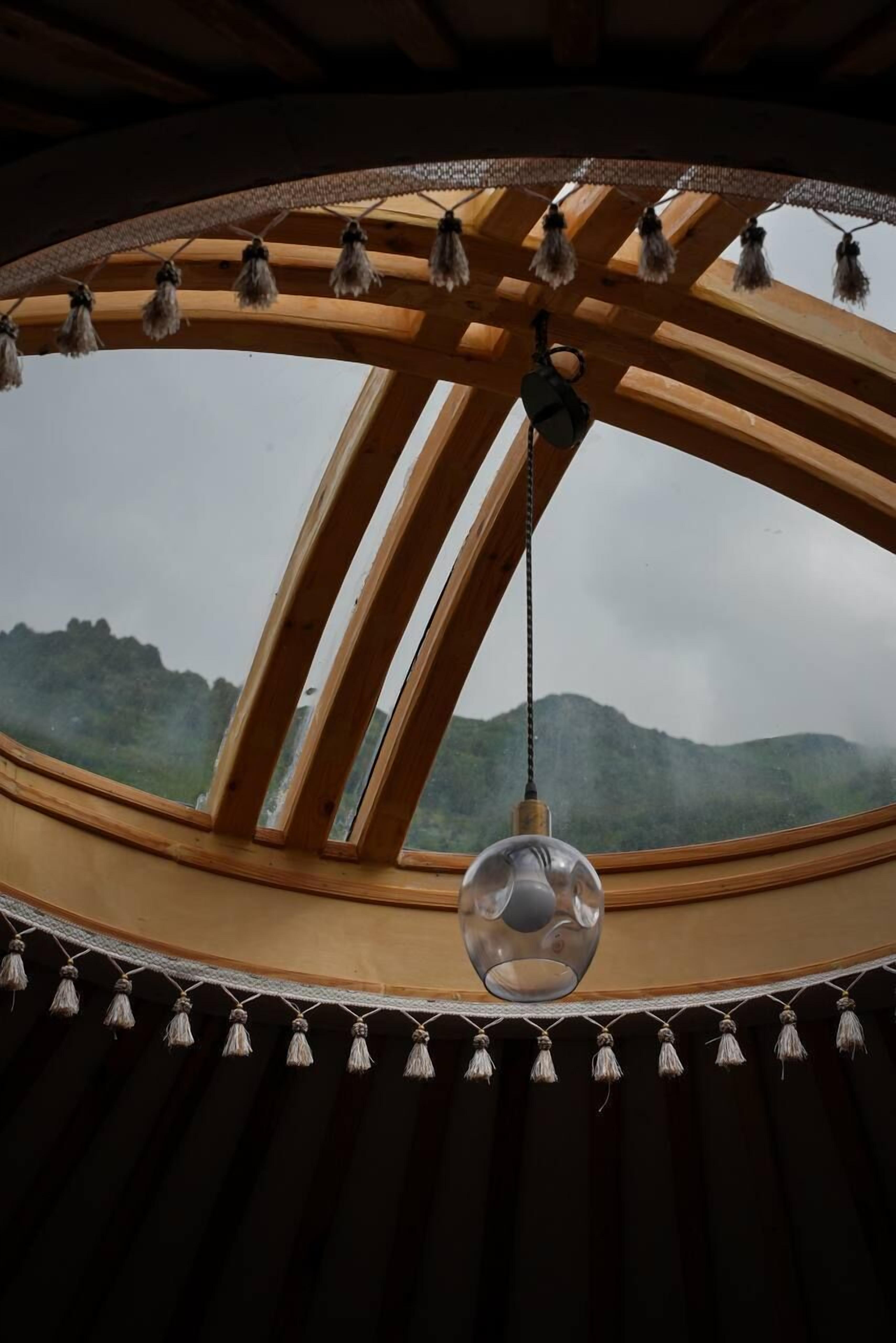 A circular skylight with wooden beams and hanging tassels, overlooking a mountainous landscape.