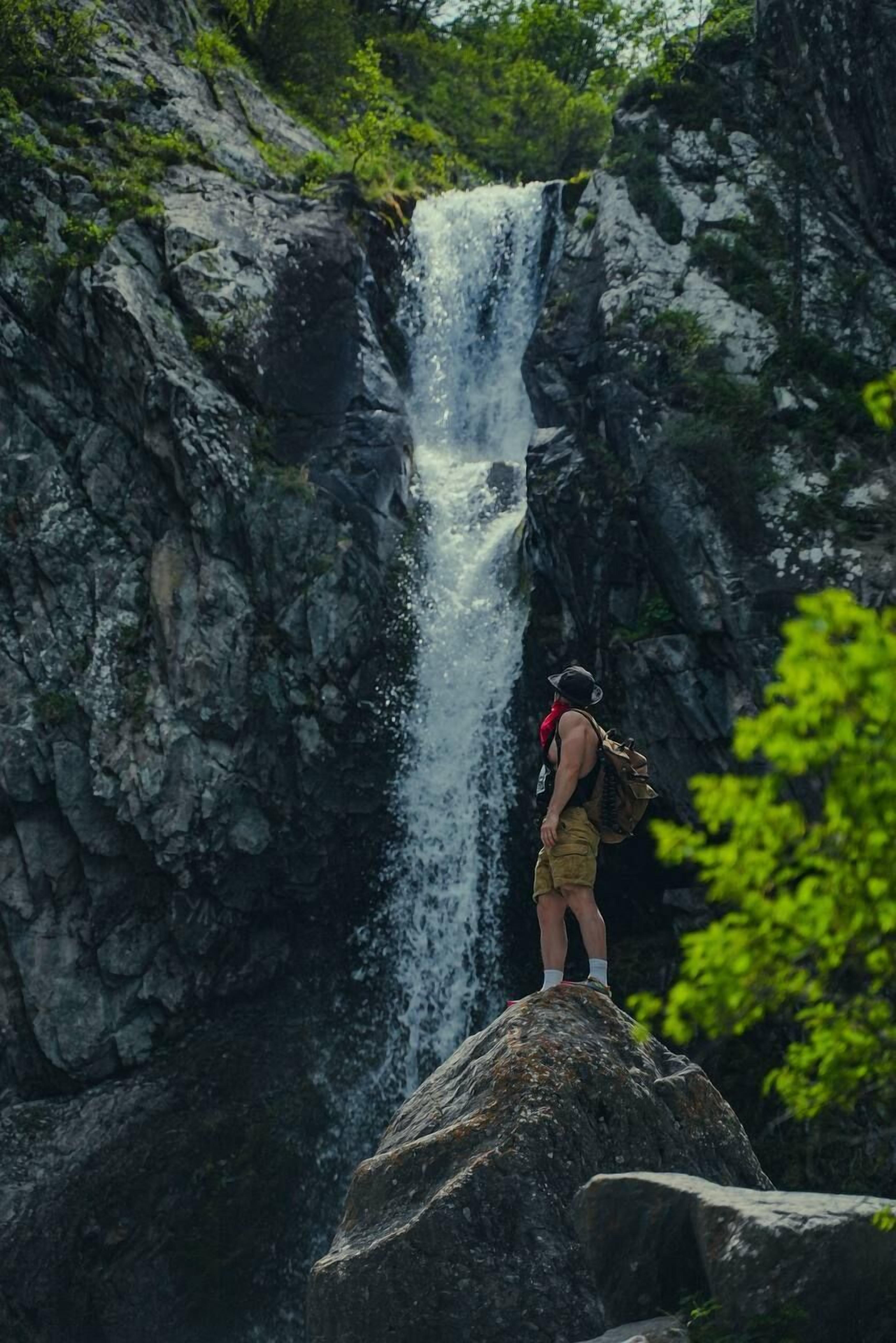 A person standing on a rock by a waterfall.