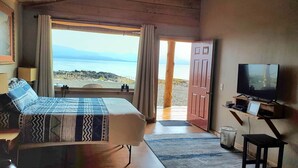 Een slaapkamer met een bed, een televisie, een bureau en uitzicht op het strand.