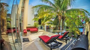 Eine moderne Außenlounge mit Glaswänden, roter Polsterung und Palmen.