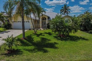 A residential house with a garage, surrounded by palm trees and a well-maintained lawn. - Villa Samba (Cape Coral)